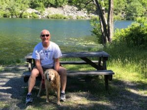 Man and a golden retriever on a picnic bench in front of a lake