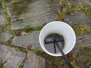 A white bucket of dirty water and brush cleaning natural stone patios