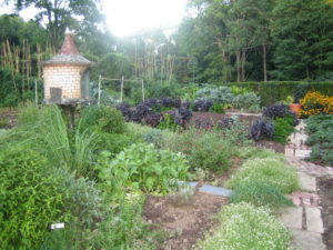 a large organic vegetable garden with a bird house and brick paths