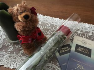 A single red rose and two bars of dark chocolate next to a teddy bear wearing heart boxers