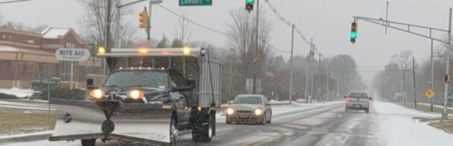 Snowy road with a truck plowing and applying road salt