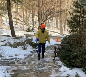 A man in a yellow jacket applying Calcium Magnesium Acetate to a natural stone patio.