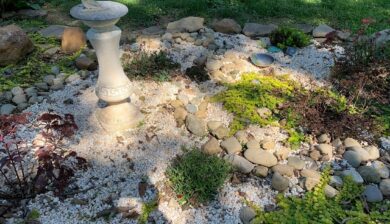 a sundial in a garden of gravel and river stone and sedum