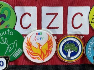 a red badge with Comfort Zone Camp logo CZC and white pin with yellow and orange Phoenix logo