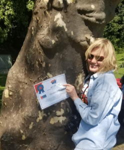 Mary Stone hugging a sycamore tree with a certificate for Best Team Name Growing Hope for Comfort Zone Camp's Grief Relief 5K