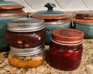 three colorful jars of hot pepper jelly on a brown marble countertop.
