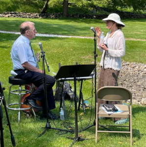 Mary Stone and Ken Roberts in a park behind a music stand and microphones