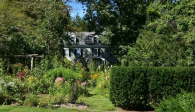 a grey farm house peaking through the gardens of Willowwood Arboretum