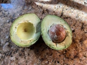 an avocado cut open on a brown granite counter