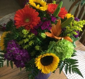 a bouquet of summer flowers including sunflowers and orange Gerber daisies.