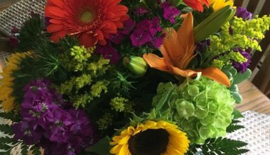 a bouquet of summer flowers including sunflowers and orange Gerber daisies.