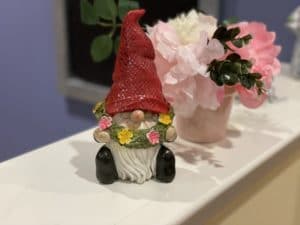 a gnome figurine with a red hat holding a floral wreath sitting on a counter top.