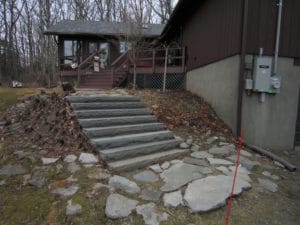 Before photo of a front walkway with a steep slope with large slabs of stone steps in front of a brown woodland house