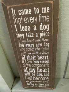 a brown wooden plaque with a a poem about losing a dog in white lettering leaning against a green wall.
