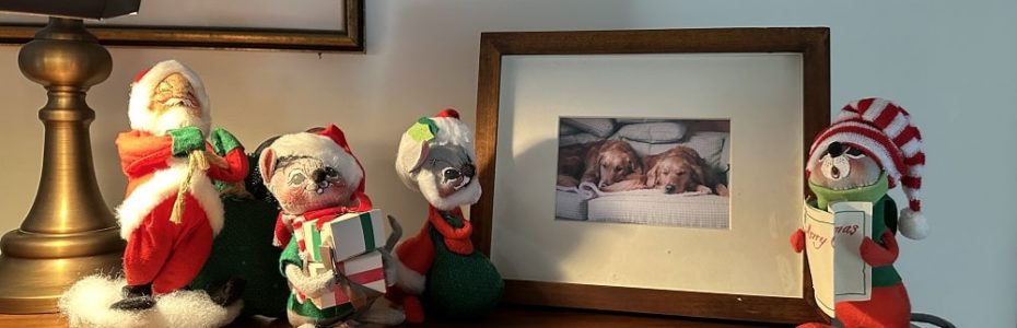 the tip of a upright piano with a framed photo pf two golden retriever pups and Analee mice dolls and Santa singing carols.