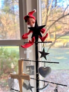 a red elf hanging from a metal Milagro Tree in a bay window.