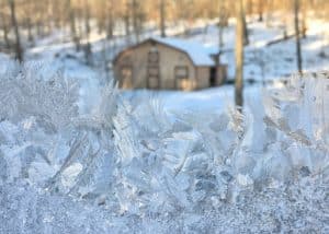 ice crystals on a widow overlooking a beige barn.