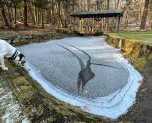 a frozen pond with a covered bridge and a. mysterious pattern in the dusting of snow.