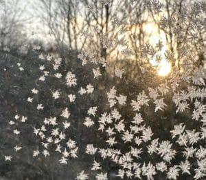 crystals on a window that look like snow flakes with the sun rising in the background.