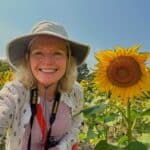 A selfie of Mary Stone smiling and wearing a beige sun hat with a happy sunflower.