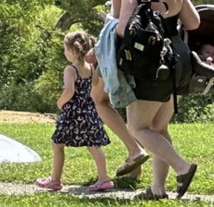 a little girl in a blue sundress and pigtails holding hands with her mom.