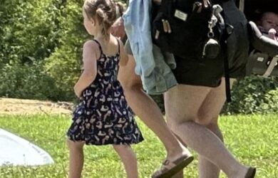 a little girl in a blue sundress and pigtails holding hands with her mom.