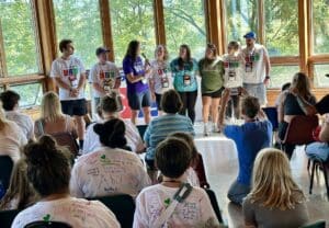 a group of Comfort Zone Camp volunteers in front of an audience of campers during a memorial serrvice.