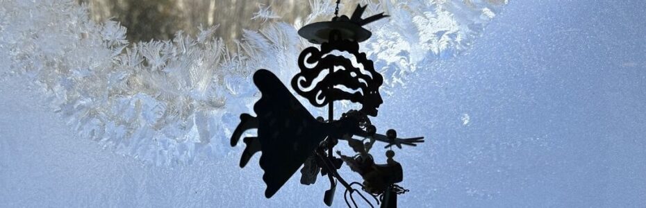 a metal ornament of a blond woman gardener in front of a window with ice crystals.