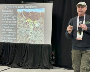 A Man in a ball cap next to a slide showing roots.