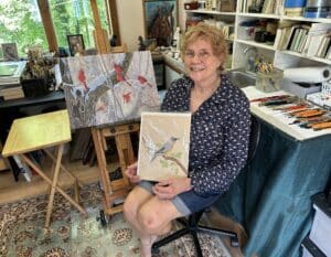 Carol Decker holding her first painting done at twelve years old.