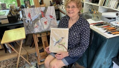 Carol Decker holding her first painting done at twelve years old.