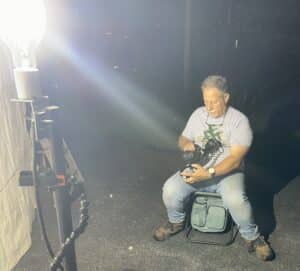 Blaine Rothhauser sititng on a camp stool looking at the viewfinder of his camera