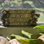 a brown plaque with flower that read Wonder is the Beginning of Wisdom