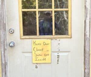 a whote door wiht yellow sign saying Keep Door Closed-Snakes Get Inside.