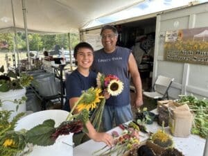 a father and son behind a table of zinnias and sunflowers making bouquets