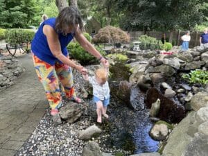 Young Thomas taking careful steps through a shallow pond while exploring a garden.