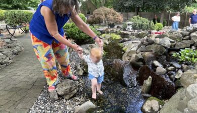 Young Thomas taking careful steps through a shallow pond while exploring a garden.