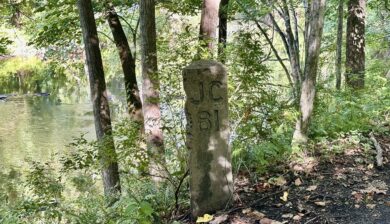 Historic JC 81 railroad milepost beside the wooded Paulinskill Valley Trail and Paulins Kill