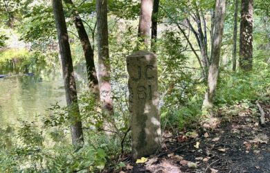 Historic JC 81 railroad milepost beside the wooded Paulinskill Valley Trail and Paulins Kill