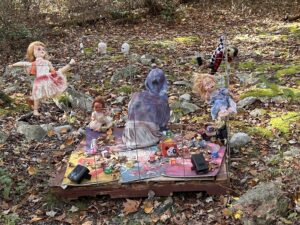 Creepy vintage dolls arranged behind wire fencing among rocks and fallen autumn leaves along the Haunted Trails at Mohican Outdoor Center.