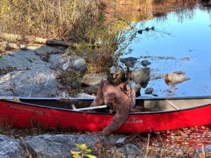 Jason Voorhees-inspired masked Halloween figure seated in a red canoe beside Catfish Pond at Mohican Outdoor Center.